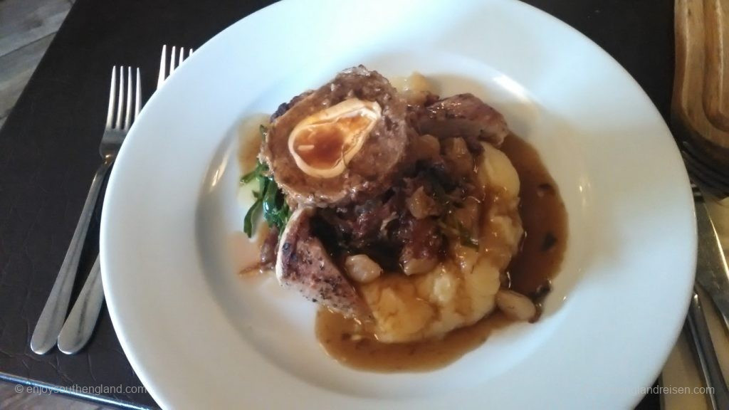 In der Pfanne gebratenes Schweinefilet an einem Scotch Egg mit Black Pudding an fein geschnittenem Schinken mit geschmorten Zwiebeln mit Schalotten-Chips und einer Rotweinsoße (Scotch Egg: Ei in einem Hackfleischmantel / Faschiertem; Black Pudding: Blutwurst / Blunzen)