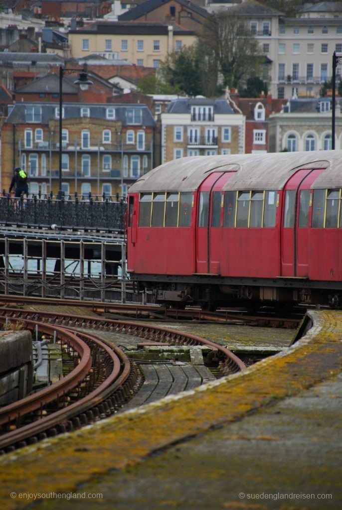 IOW Island Line - Ausfahrt aus dem Bahnhof Ryde Pier Head. Im Hintergrund die Stadt und zwischen Zug und Hintergrund die Fußgängerbrücke auf den Pier. Schön zu sehen auf dem nur in Ausnahmefällen genutzten linken Gleises die freiliegende Stromschiene.